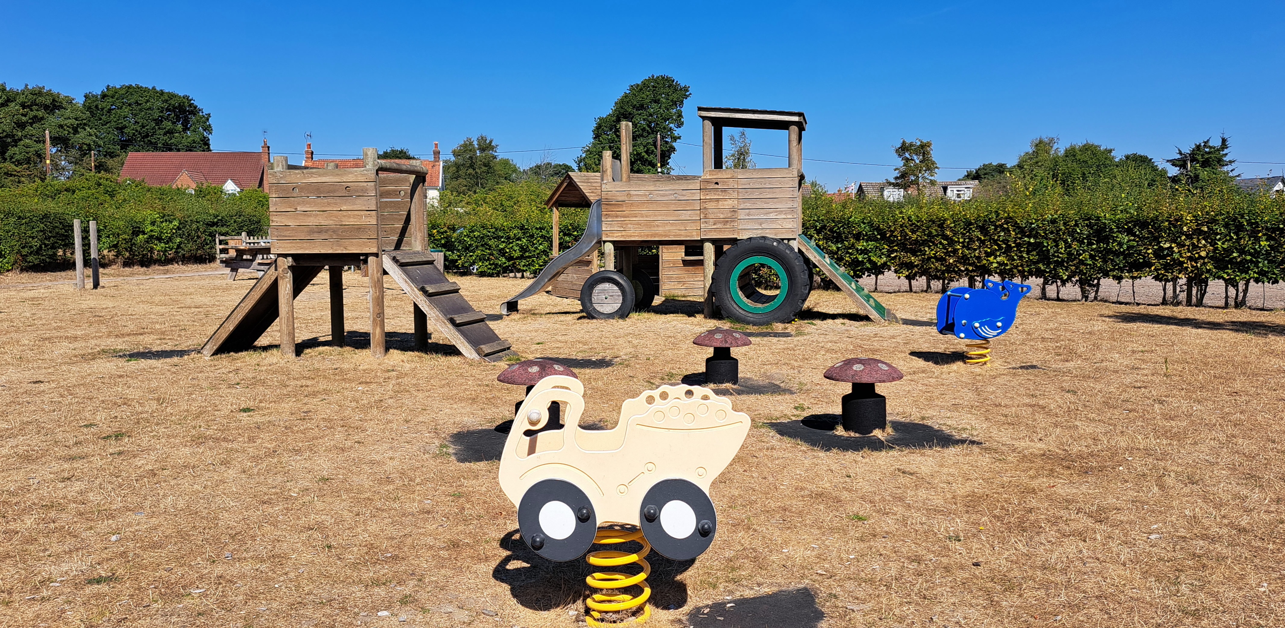 August 2022. Parched earth and play equipment. Houses in background