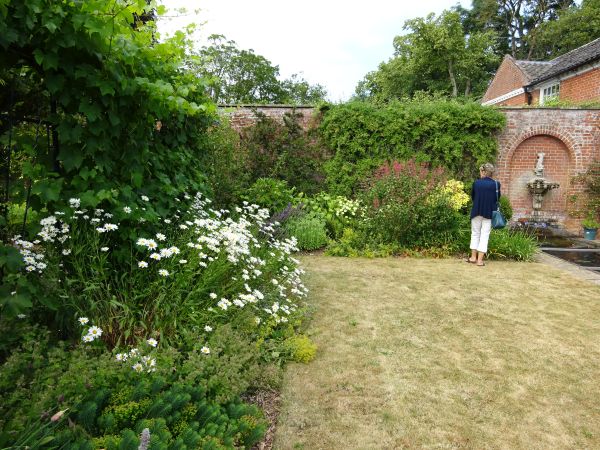 Lawn with flower beds to left and water feature in brick wall and visitor at rear.