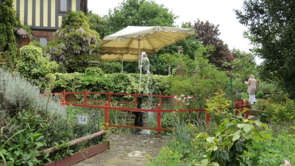 Fence water feature with shrubs surrounding and large sun canopy at rear.