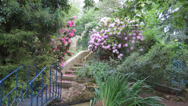 Blue metaf footbridge leading to stone footbridge through shrubs