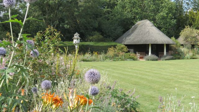 Lawn with flower beds and thatched shelter.