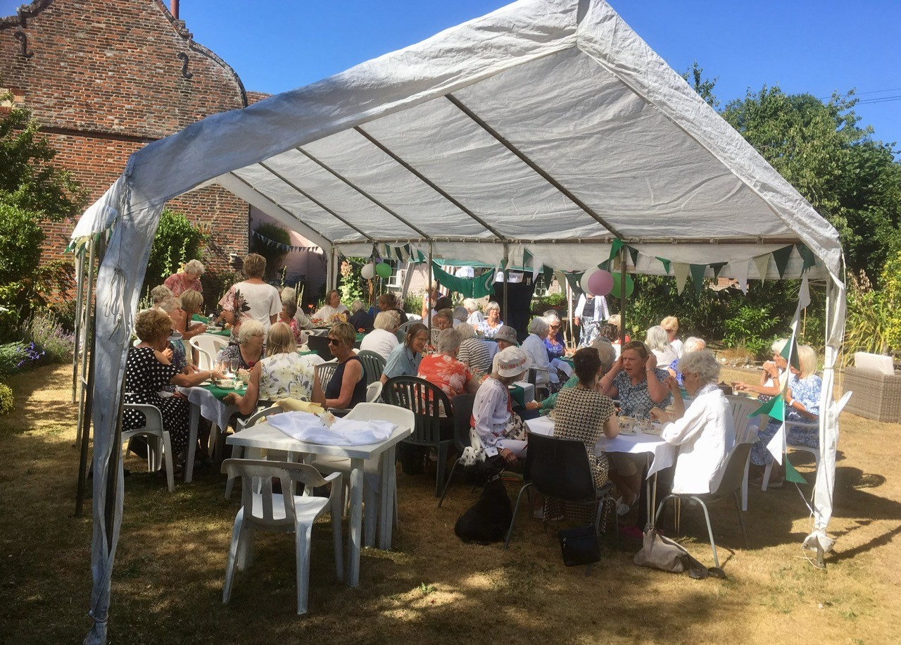 WI Members taking tear under awning in garden.